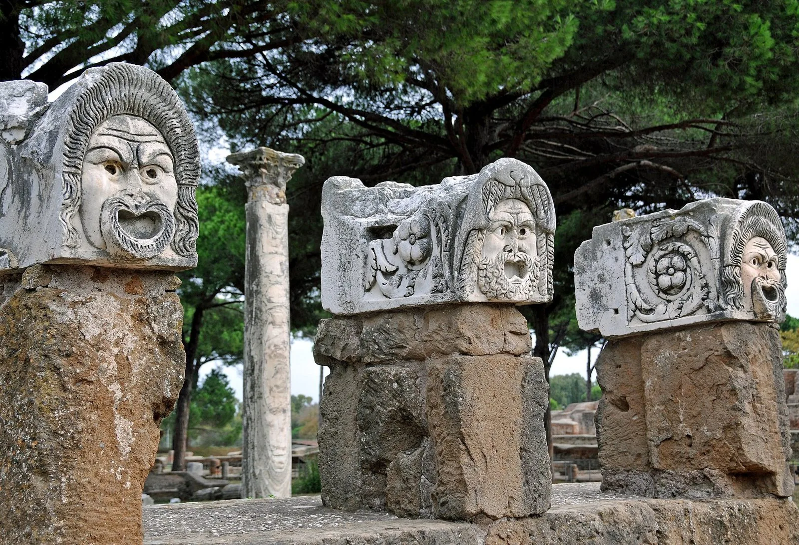 Maschere teatrali in marmo esposte presso il Teatro Romano di Ostia Antica, tra pini e colonne
