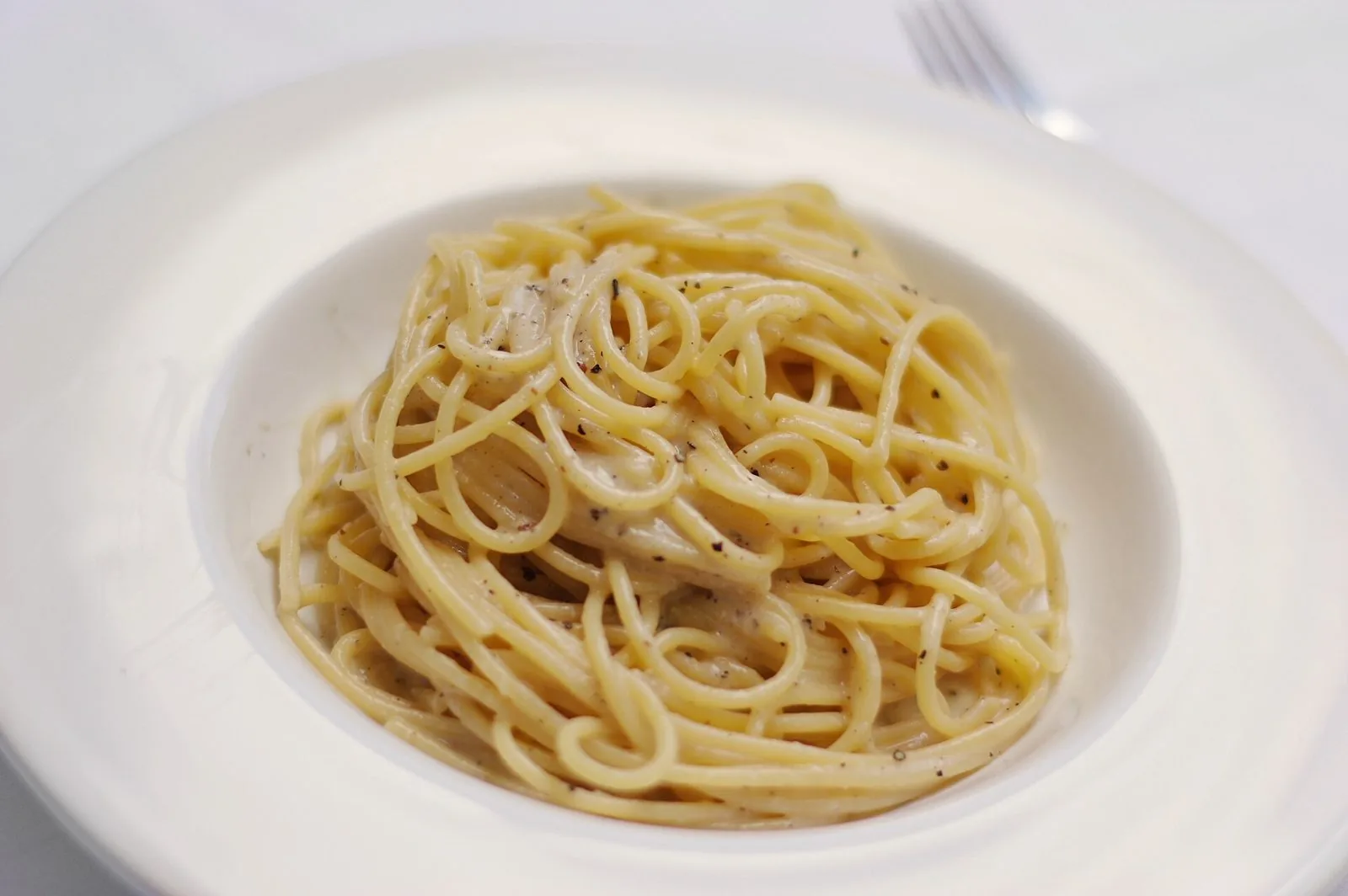 Piatto di spaghetti cacio e pepe cremosi in un piatto fondo bianco
